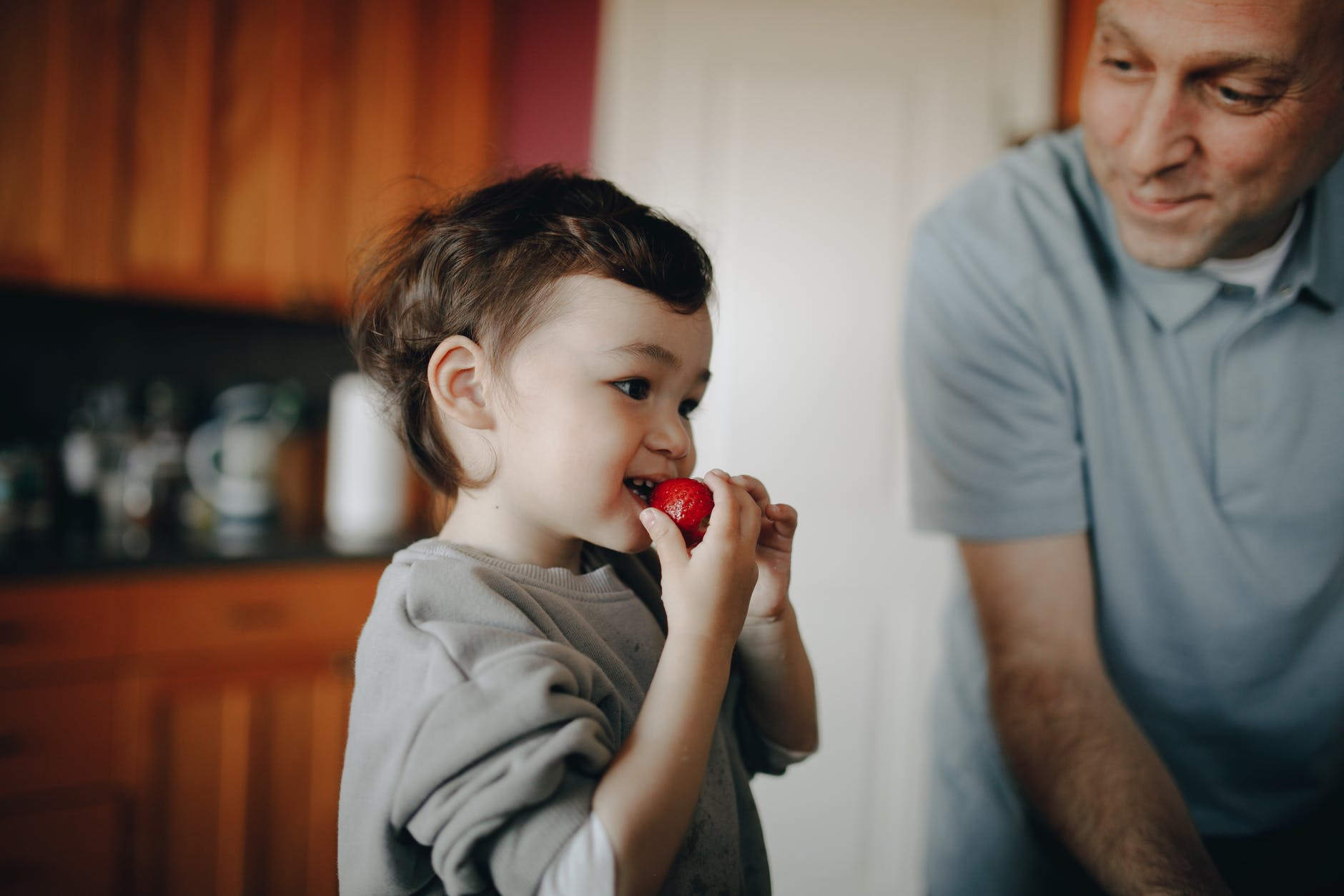 a child eating strawberry beside her father