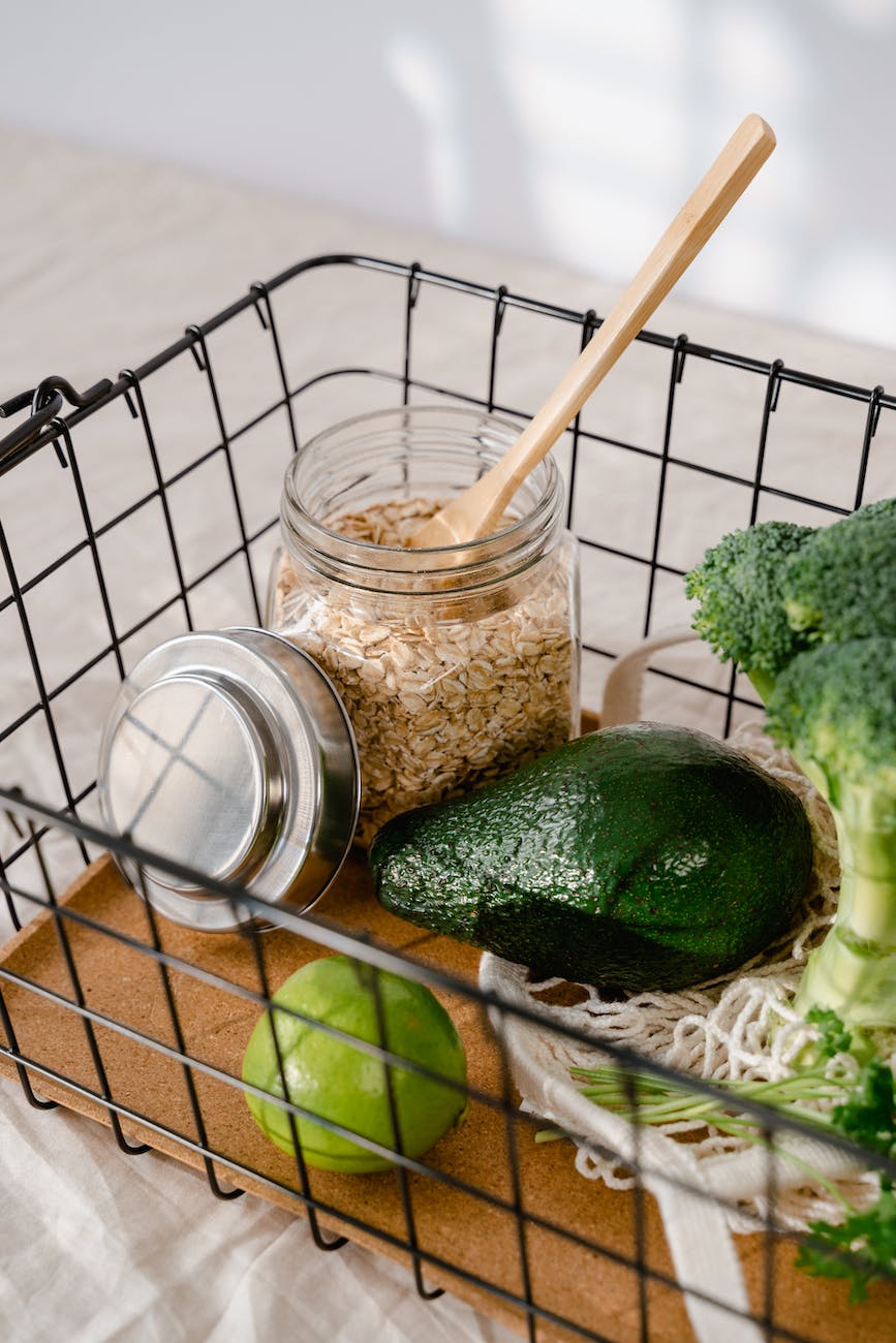 a basket with a wooden spoon in a jar of oatmeal beside an avocado and a lime